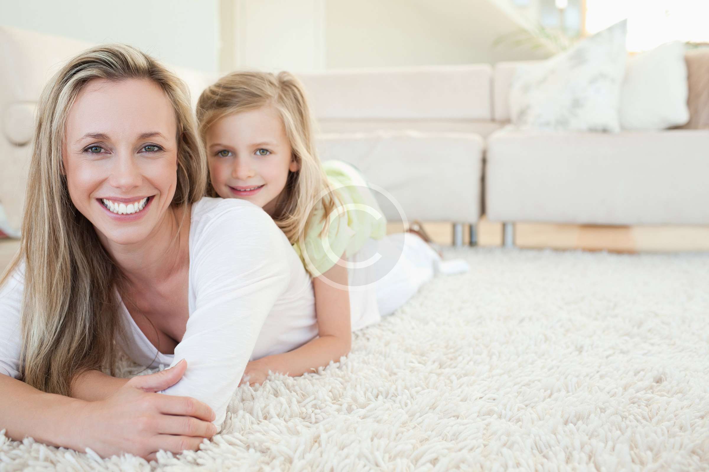 A woman and her daughter peacefully lounging on a white carpet.